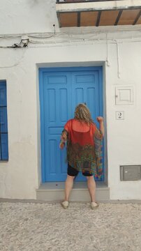 Woman knocking on a bright blue door in a traditional village street