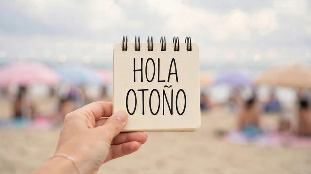 Woman holding a small notepad with the message Hola Oto&ntilde;o on a sunny beach, concept of seasonal transition from summer to autumn