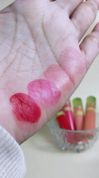 Vertical close up of cotton pad wiping colorful lipstick stains from hand. Beauty cosmetic cleansing concept, makeup removal process.
