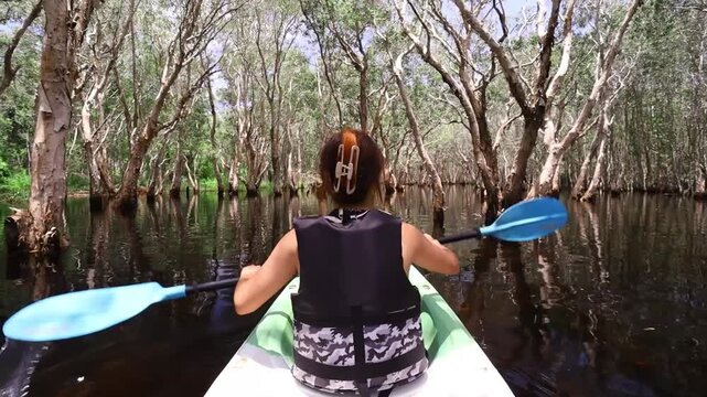 Asian female tourist happily kayaking amidst green nature and bright blue sky in Rayong Botanical Garden, Rayong province, Thailand.
