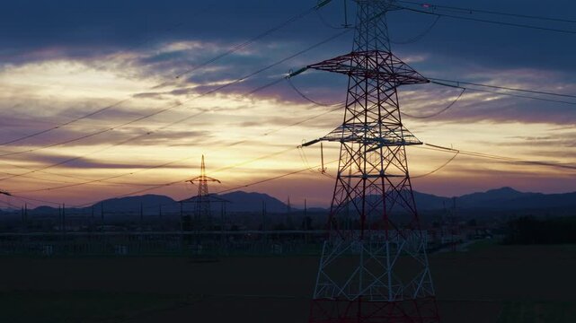 Crane of High-voltage electrical substation switchyard shows transformers and transmission lines during dramatic sunset sky in a rural area.