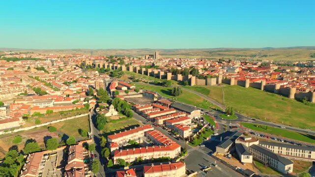 Rows of townhouses near Avila, Spain, line a quiet road beside open green fields.