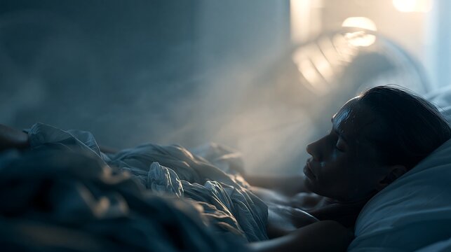 Woman sleeping in a hot bedroom during a tropical night, struggling with heat stress despite an electric fan, illustrating insomnia, overheating and climate change with copy space