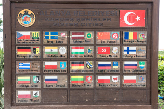 Signboard displaying sister city flags and names in Alanya, Turkey, featuring various international flags and city names in multiple languages