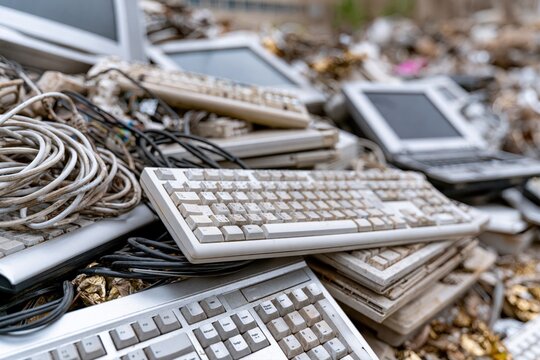 Pile of obsolete and discarded computer hardware, including keyboards, monitors, and laptops, representing e-waste.