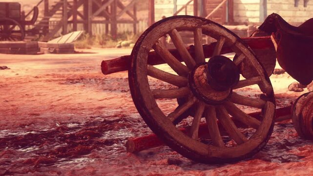 A wooden wagon wheel lies on the ground in a town. The sun sets in the background, creating shadows. Dust and remnants of a busy day cover the earth. Signs of past activity are present.