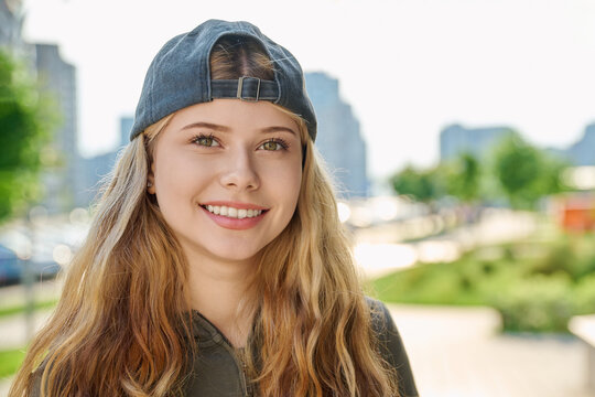 Portrait of pretty smiling blonde teen girl wearing backward baseball cap outdoors