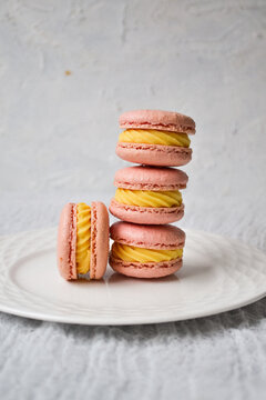 Stack of pink French macarons with yellow cream filling on a white plate