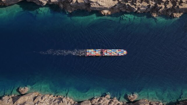 Top down container ship crossing narrow rocky coastal strait