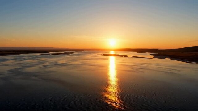 Aerial view of golden sunset reflecting on calm river with sandbars and distant hills
