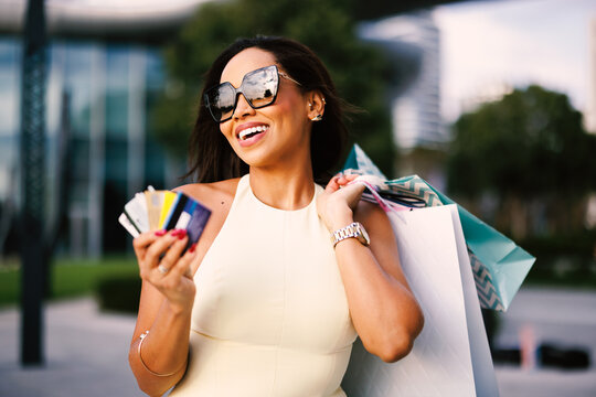 Smiling Latin American woman holding credit cards and shopping bags after a shopping trip outdoors