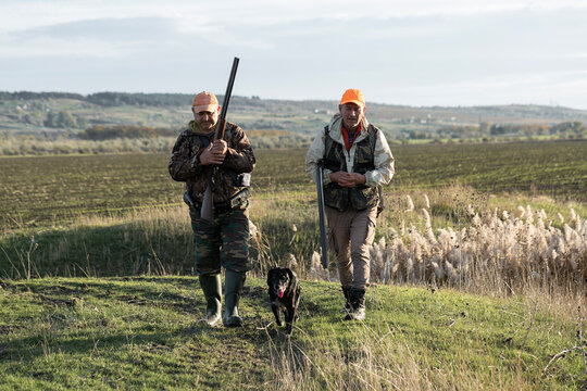 A hunters in camouflage clothing with a gun in his hands walks along the reeds.