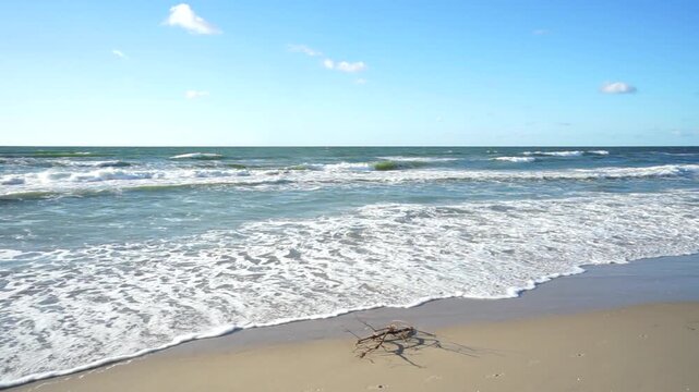 Waves rolling onto a sandy Baltic Sea beach on a sunny summer day. Rough water, white foam and blue sky create a beautiful coastal landscape with a peaceful yet dynamic seaside atmosphere.