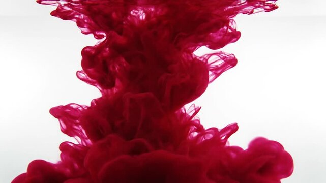 Deep red ink swirling and diffusing in clear water on white background