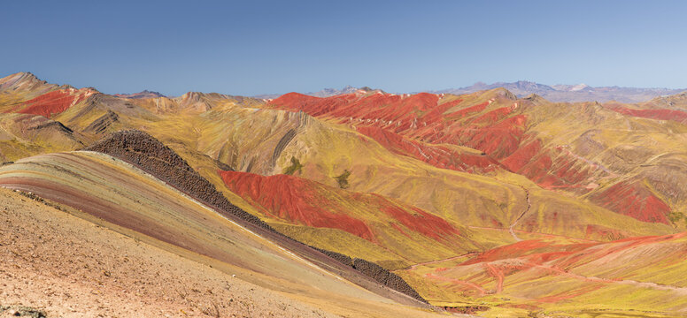 Wide panoramic view showcasing the vibrant red, yellow, and striped mineral layers across the mountain slopes of the Palccoyo Rainbow Mountain range in Peru