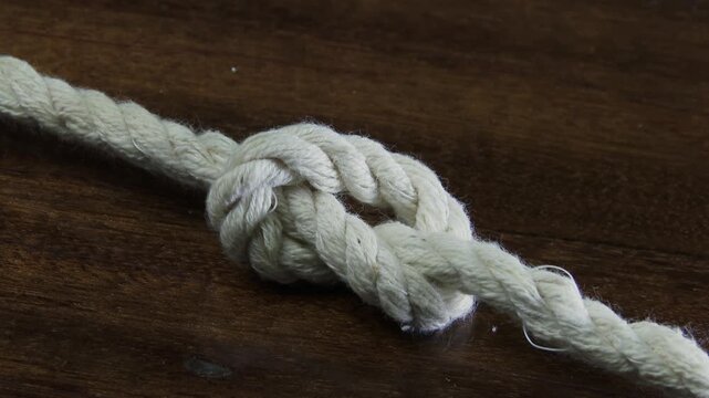 White rope tightening into a knot on a wooden surface.