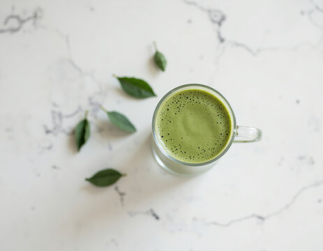 Top View Flat Lay of Matcha Green Tea Latte Glass Cup with Fresh Green Leaves on White Marble Table