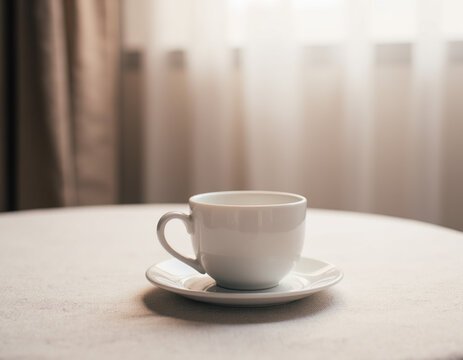 Classic White Ceramic Coffee Cup and Saucer Standing on Linen Tablecloth in Soft Window Sunlight