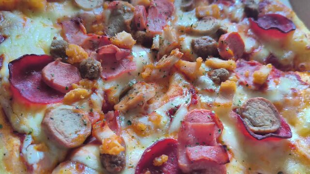 Macro camera shot moving over a hot baked pizza topped with sausage, pepperoni, ham, and melted mozzarella cheese.