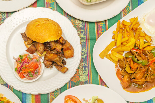 Close-up of chicharr&oacute;n bread with tomato salsa beside a hearty peppered meat and fries dish, framed by patterned fabric.