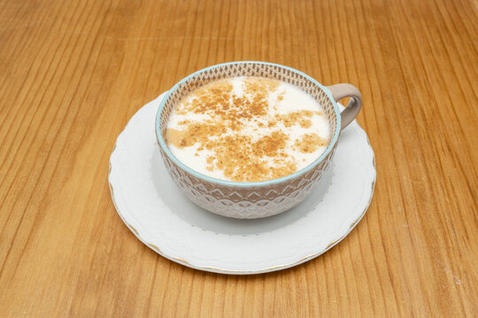 Creamy morocho drink dusted with cinnamon, served in a textured teal-rimmed cup on a wooden table.