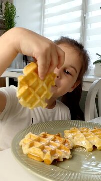 A beautiful young girl-child eats Belgian waffles with a happy face, smiles and laughs.