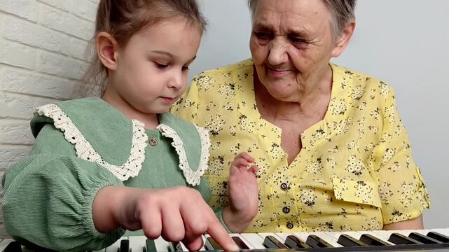 Elderly grandmother teaching little sweet girl playing piano, smiling with happiness, staying at cozy home, spending time together. Family, Love, Education Concept.