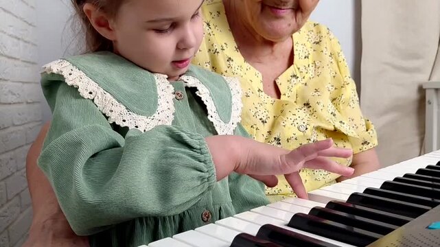 Elderly grandmother teaching little sweet girl playing piano, smiling with happiness, staying at cozy home, spending time together. Family, Love, Education Concept.