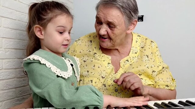 Elderly grandmother teaching little sweet girl playing piano, smiling with happiness, staying at cozy home, spending time together. Family, Love, Education Concept.