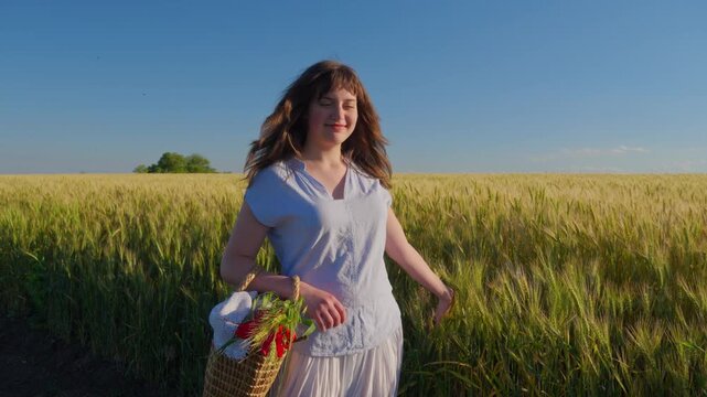 A happy teenage girl in a white summer outfit carrying a wicker basket filled with red poppy flowers while walking through a golden grain field under a blue sky