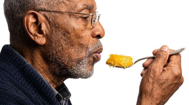 Senior man tasting food with a spoon. Elderly gentleman sampling a bright yellow dish in natural light.