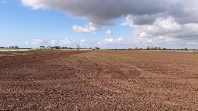 Plowed farmland. First keyframe shows expansive brown soil with tractor tracks under a cloudy sky. Second keyframe captures close-up soil texture