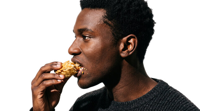 Young man eating a sandwich on the go. African American male enjoying quick lunch outdoors in natural light.