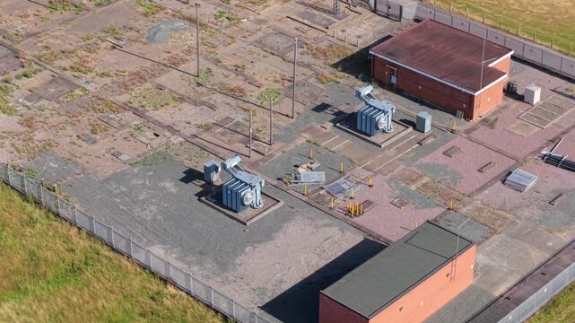Detailed aerial close up view of twin step down power transformers with rotating cooling fans and distribution lines