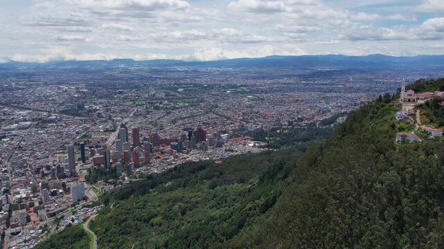 Drone flies toward Bogot&aacute; skyline from a forested hillside with Andean mountains beyond.