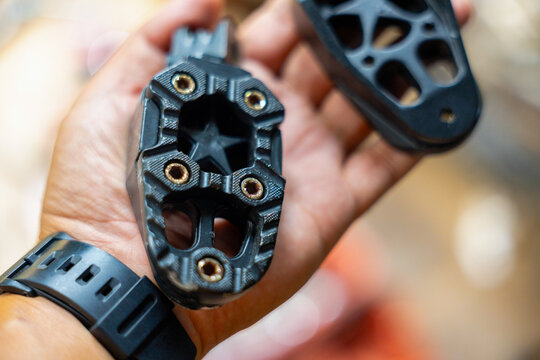 Black plastic bicycle pedal with metal threaded inserts held in hand, closeup showing texture, wear and watch on wrist conveying practical repair and outdoor gear use