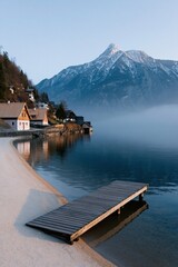 Fototapeta premium Small dock and lakeside cottages with snowcapped mountain backdrop at sunrise for vertical wallpaper and tranquil travel design