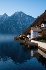 Fototapeta premium Serene waterfront houses by a reflective mountain lake with clear sky and soft morning light for background and travel banner design
