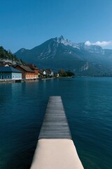 Fototapeta premium Centered wooden jetty leading into alpine lake with mountain skyline for minimalist wallpaper and poster design