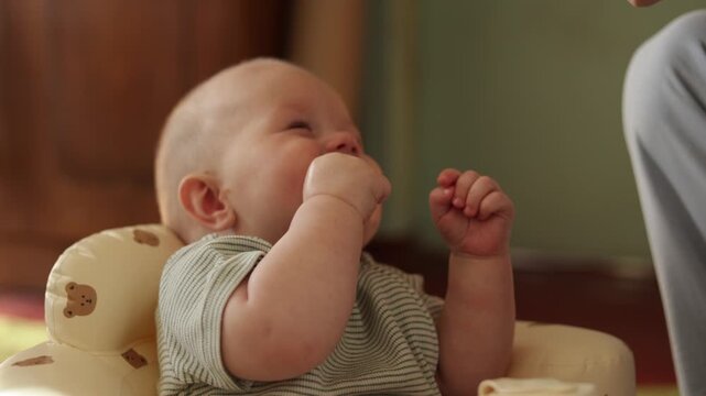 Adorable baby in a booster seat exploring their hands and mouth with curiosity