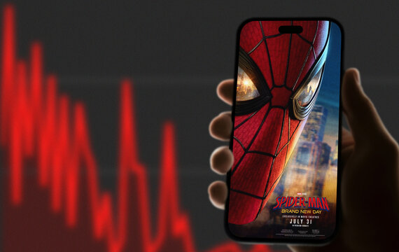 Spider-Man Brand New Day Movie Poster Displayed on Smartphone Case Held in Hand Against Declining Stock Chart Background