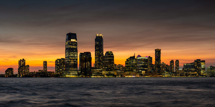 Downtown Jersey City skyline and Exchange Place at sunset with illuminated skyscrapers along the Hudson River. New Jersey, USA