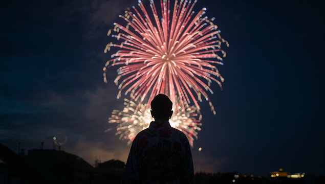 夏の夜空に大きく打ち上がる大輪の華やかな花火をあおぎ見る和装・浴衣姿の人物のシルエット