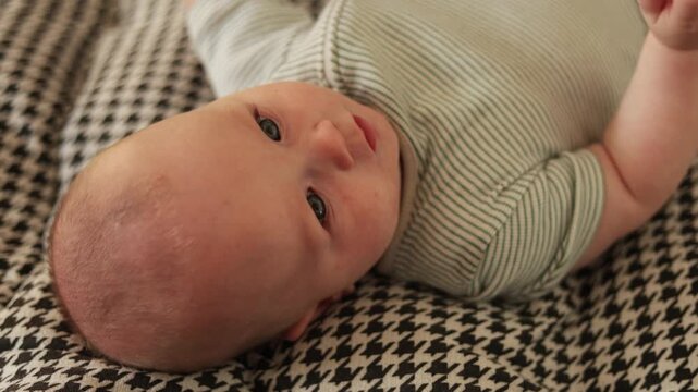 Adorable baby with blue eyes and a gentle smile lying on a patterned blanket
