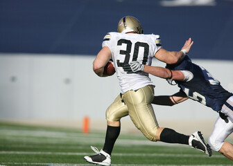 Fototapeta premium Dynamic American Football Action: Player in White and Gold Uniform with Number 30 Running with the Ball while Evading a Tackle from a Navy‑Blue‑and‑White Opponent