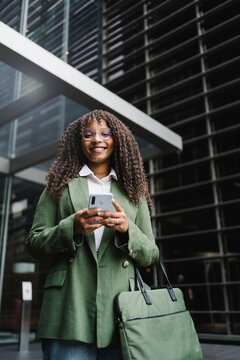 Young happy confident business woman standing on corporate street using mobile phone app