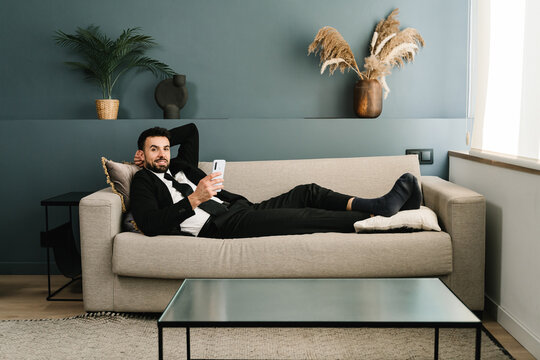 Portrait of young elegant businessman wearing a suit relaxing lying on a couch at home
