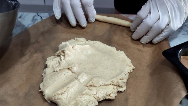 watching dough being rolled out with a rolling pin on a wooden surface in a kitchen setting with neutral mood and top-down view, baking food preparation scene with flour and brown color.
