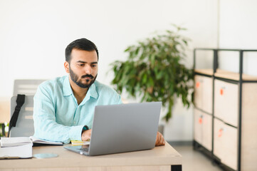 Fototapeta premium Indian man working on laptop in modern office