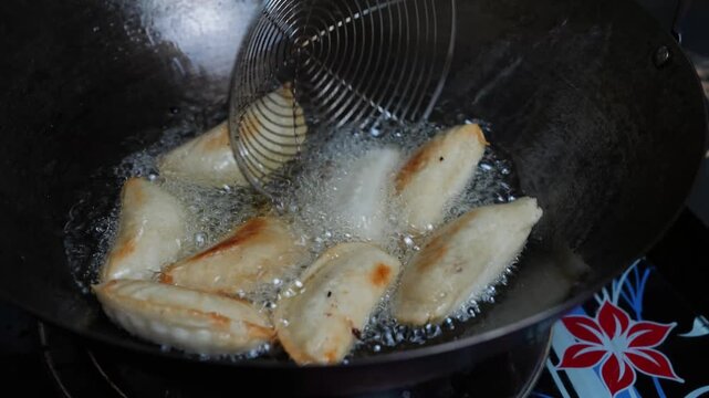 Close-up of dumplings frying in hot oil in a wok with a metal skimmer, showing home cooking and crispy golden food preparation